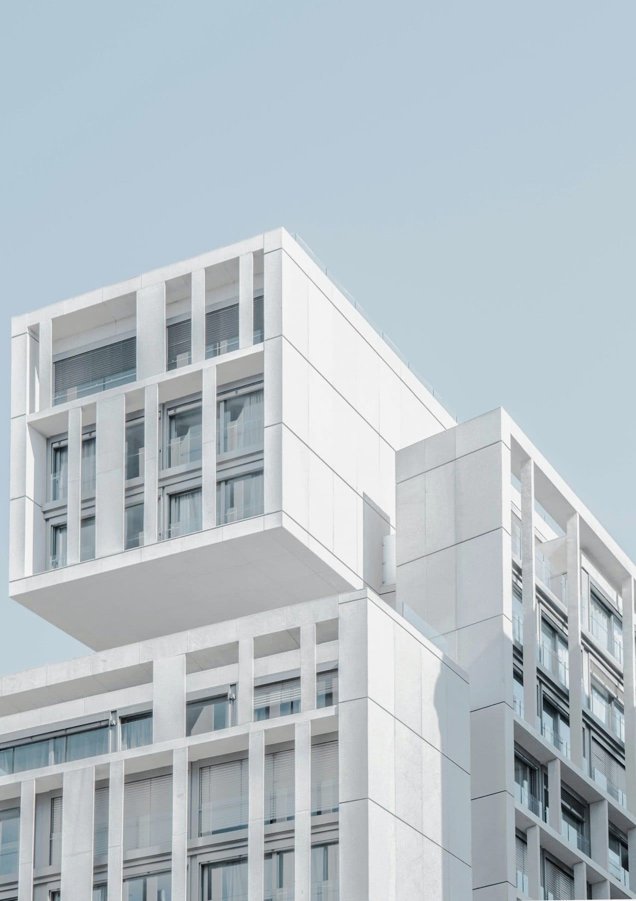 Cantilevered white housing block against a hard sky.