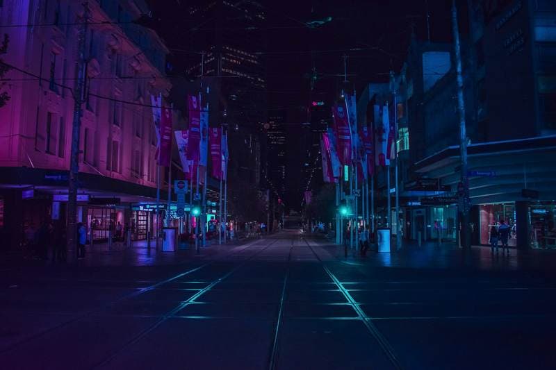 Empty night street, tram lines, magenta and cyan shop light.
