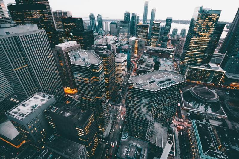Aerial city at dusk, windows starting to switch on.