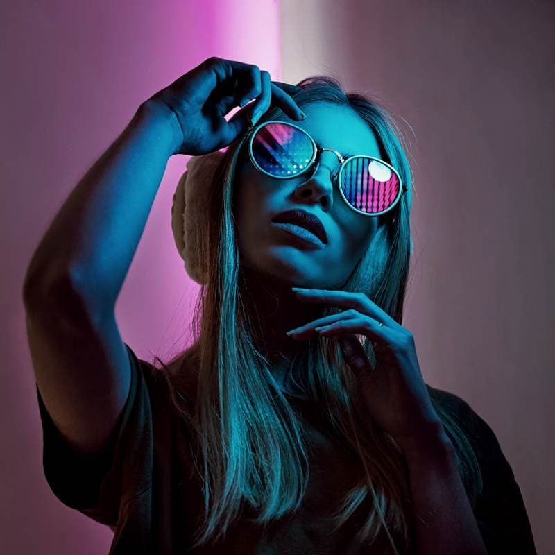 Round sunglasses and earmuffs catching pink and cyan light.