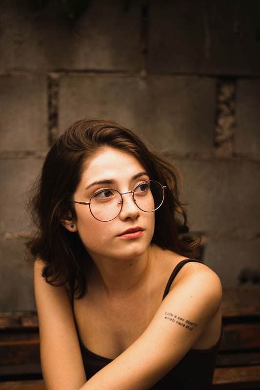 Round glasses, cinder-block wall, a tattoo on the upper arm.