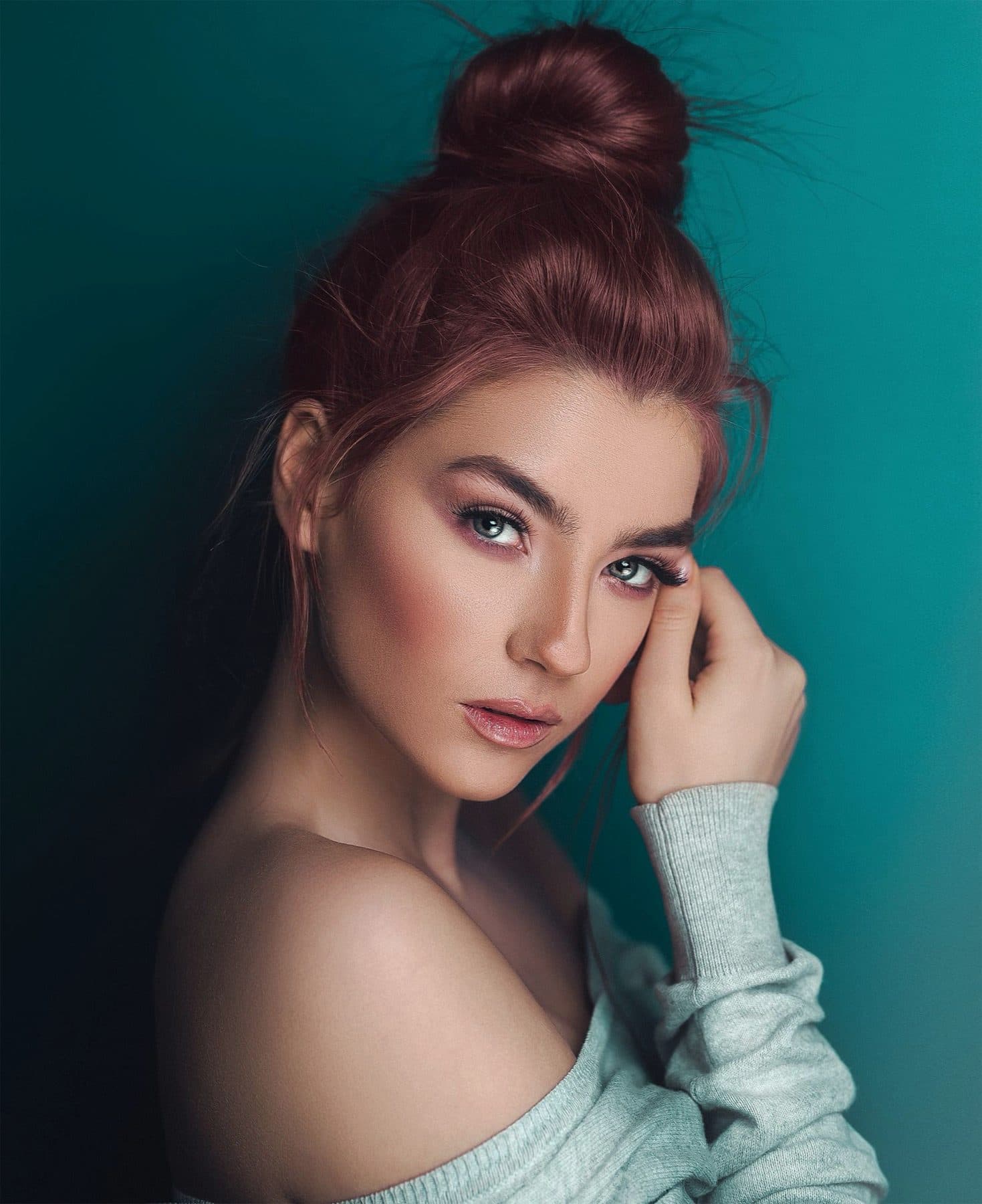 Off-shoulder grey knit against a teal wall.